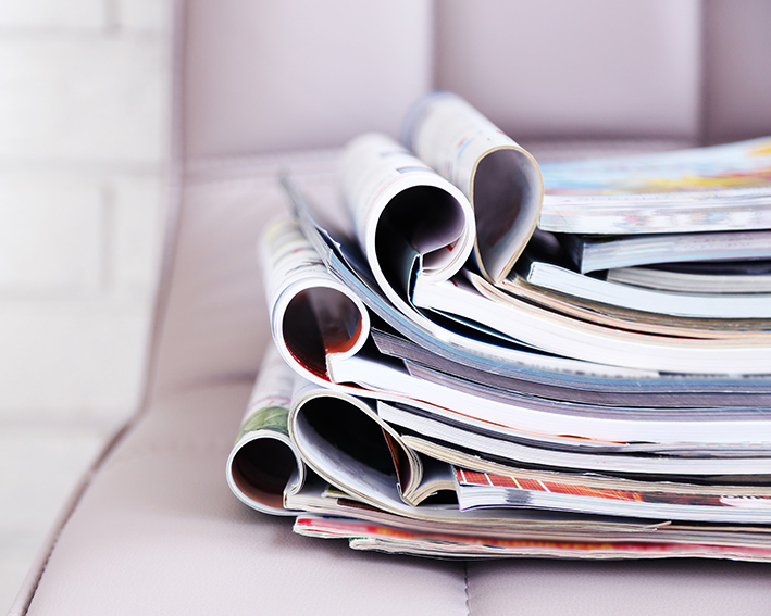Pila de revistas dobladas apiladas sobre un sillón, simbolizando recursos de lectura e información.