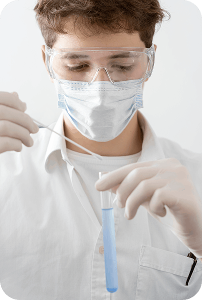 Joven técnico de laboratorio con mascarilla y gafas protectoras, manipulando un tubo de ensayo con líquido azul.